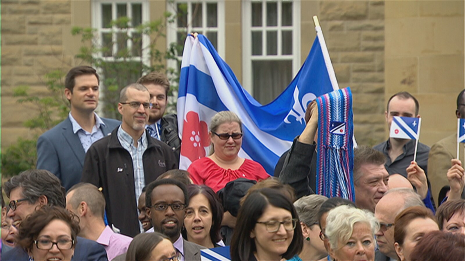 Des francophones brandissent des drapeaux franco-albertains à l'extérieur d'un bâtiment officiel.