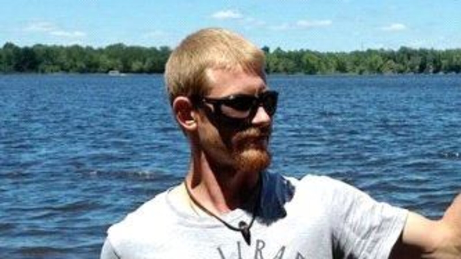 Un homme avec des lunettes de soleil pose pour une photo près d,june rivière en été.