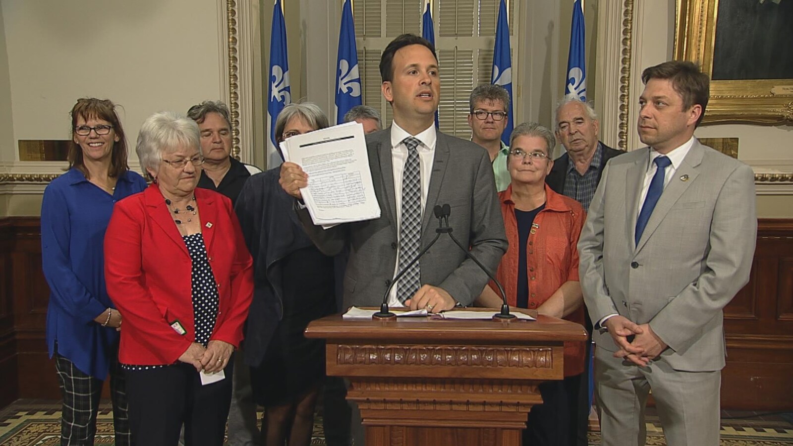 Alexandre Cloutier montre la pétition entouré des élus et militants dans le hall du Parlement.