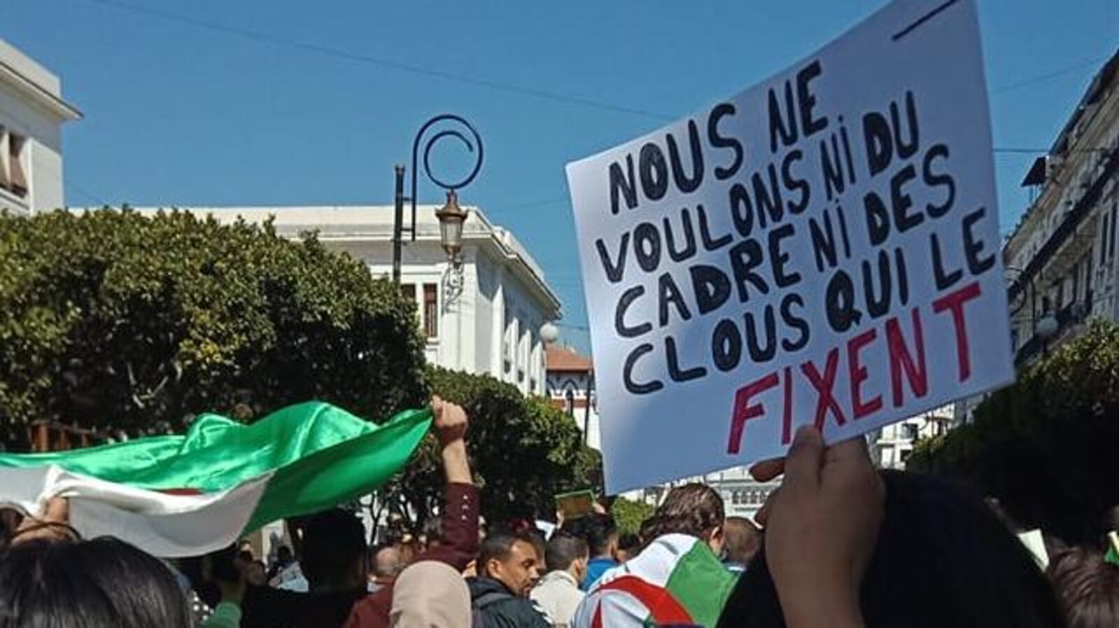 Un manifestant tient une pancarte sur laquelle on peut lire : « Nous ne voulons ni du cadre ni des clous qui le fixent ».