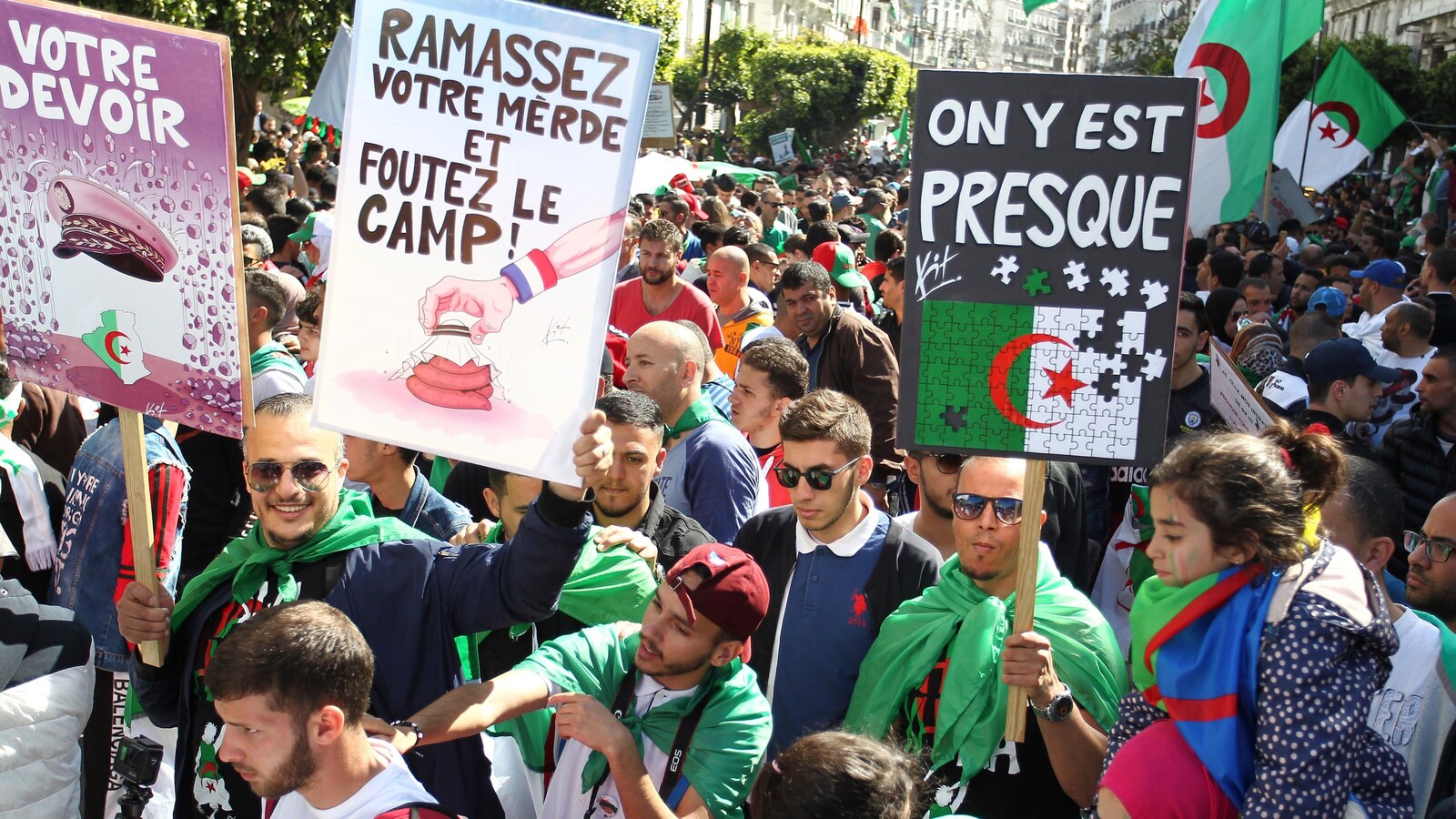 Des manifestants brandissent des pancartes au milieu d'une foule. « Ramassez votre merde et foutez le camp », peut-on lire sur l'une d'elles.