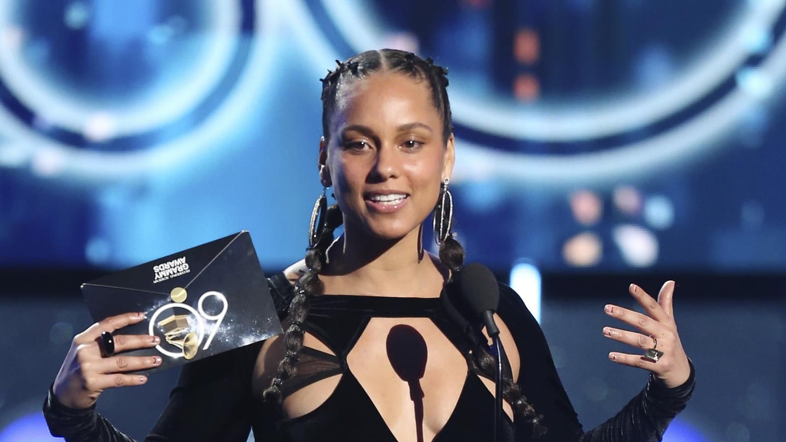 Alicia Keys s'exprimant sur une scène. Elle porte une robe noire et a une enveloppe des Grammy Awards dans sa main droite.