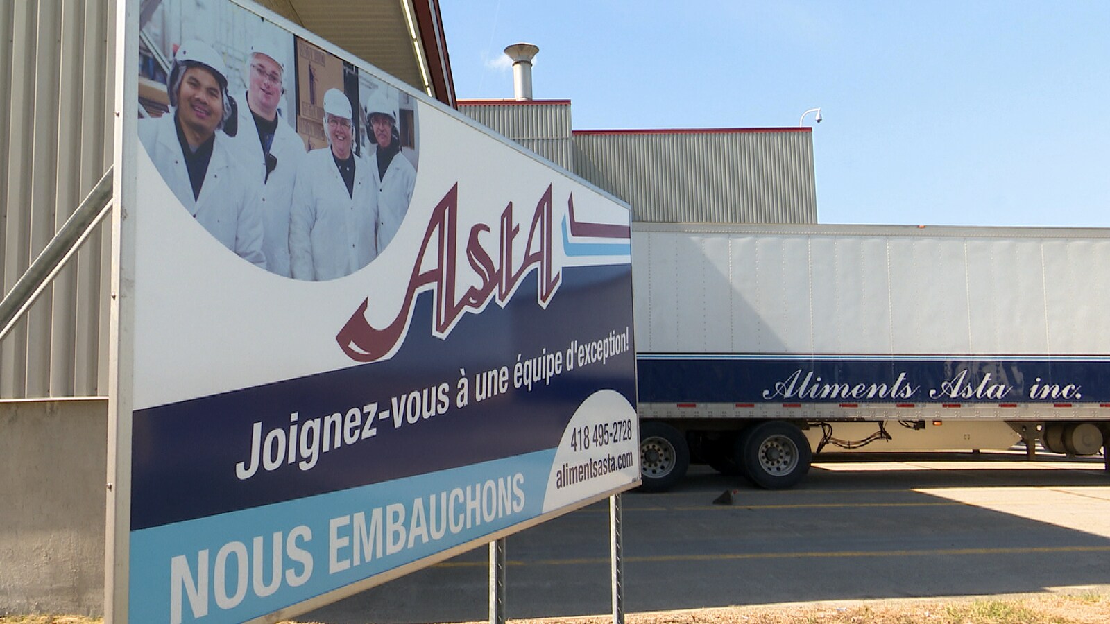Une affiche d'Aliments Asta et une remorque de livraison stationnÃ©e prÃ¨s de l'entreprise