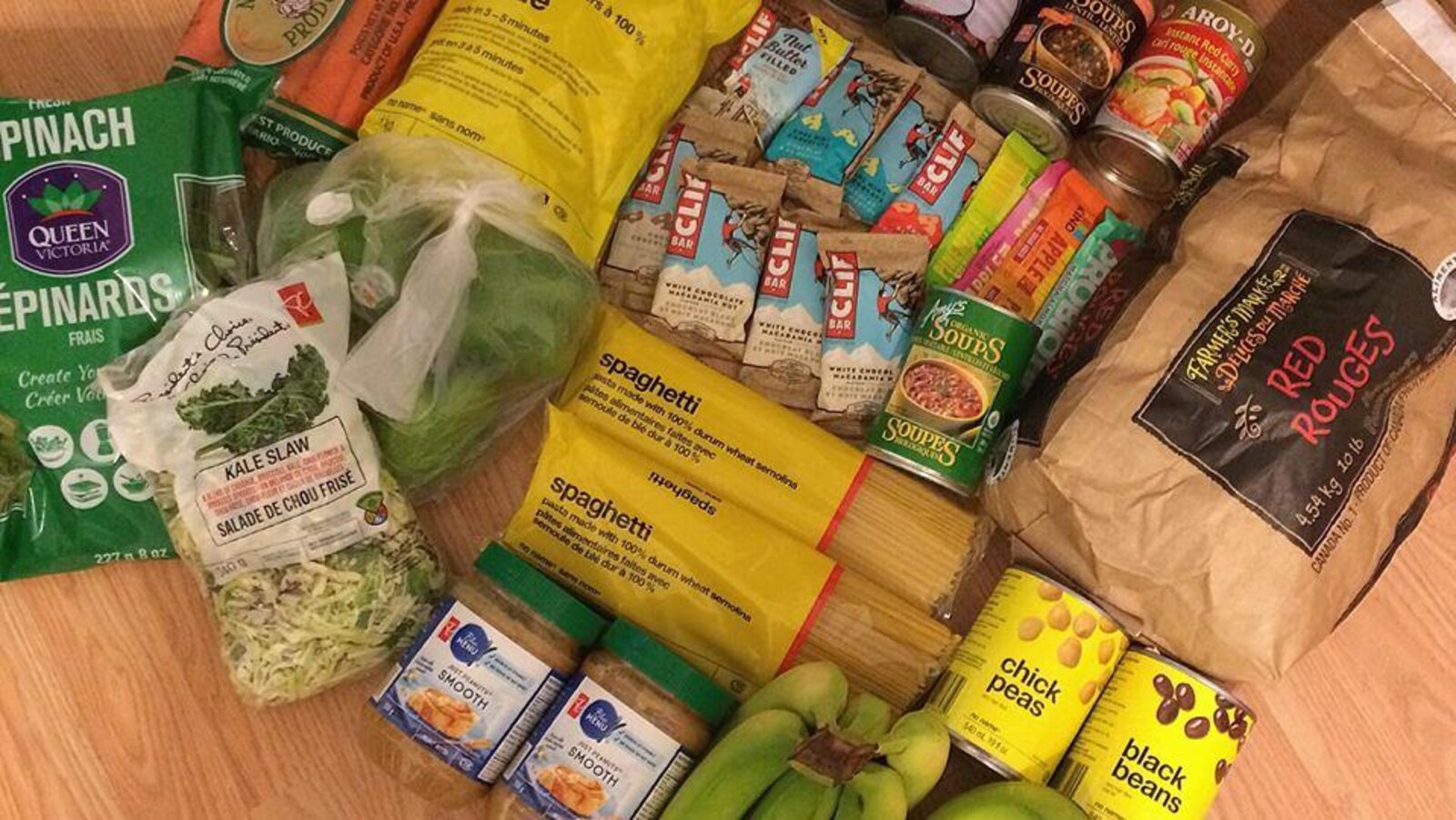 Plusieurs aliments alignés sur le sol pour une photo, comme des bananes, des pâtes, du beurre d'arachide et des barres tendres.