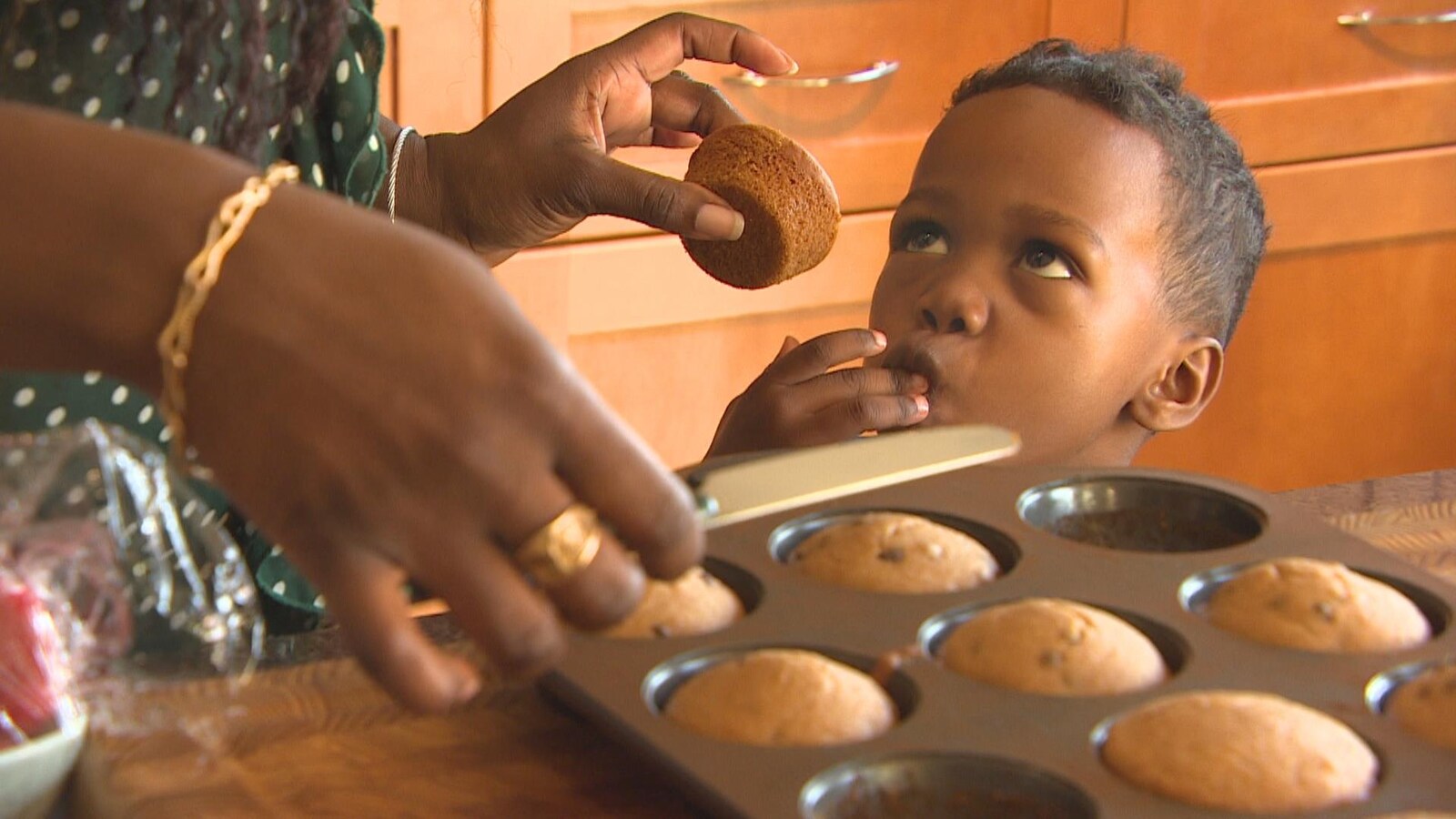 Un jeune garçon se lèche les doigts tandis que sa mère lui tend un muffin sorti du four.