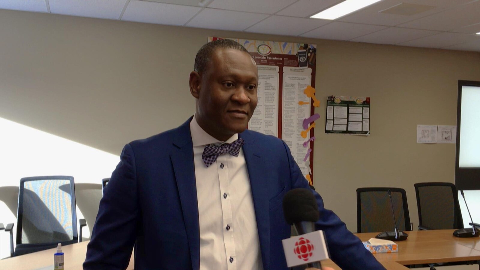 Un homme debout dans une salle avec des tables et des chaises s'adresse au micro de Radio-Canada.