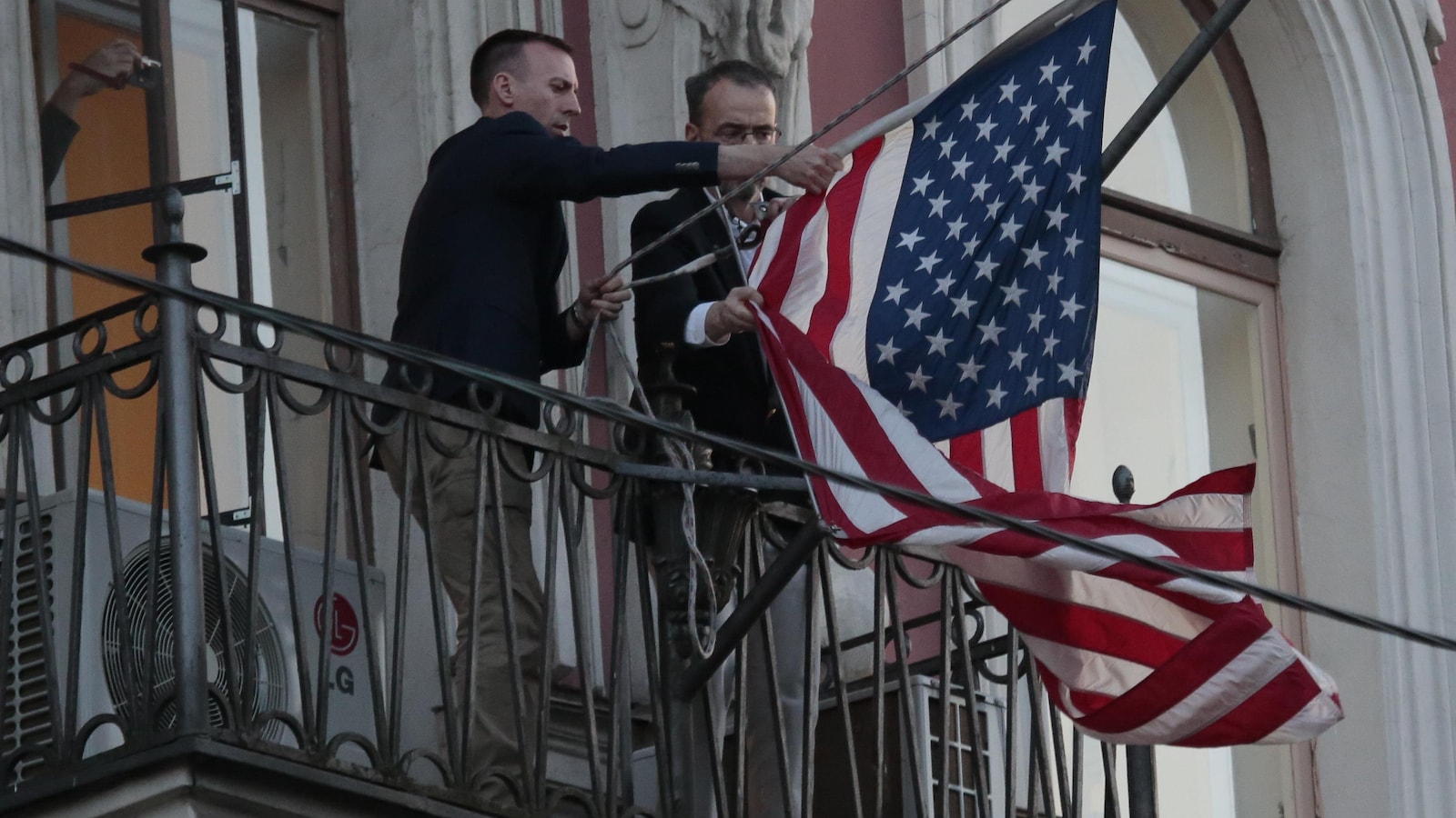 Des employés du consulat des États-Unis à Saint-Pétersbourg retirant le drapeau américain du fronton.