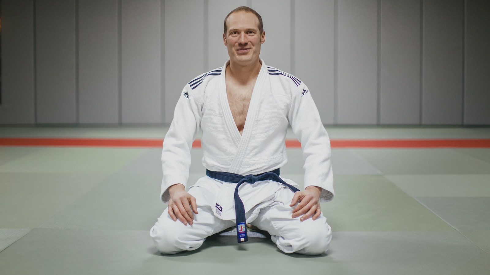 Un homme dans un habit d'art martial est à genoux dans un gymnase.