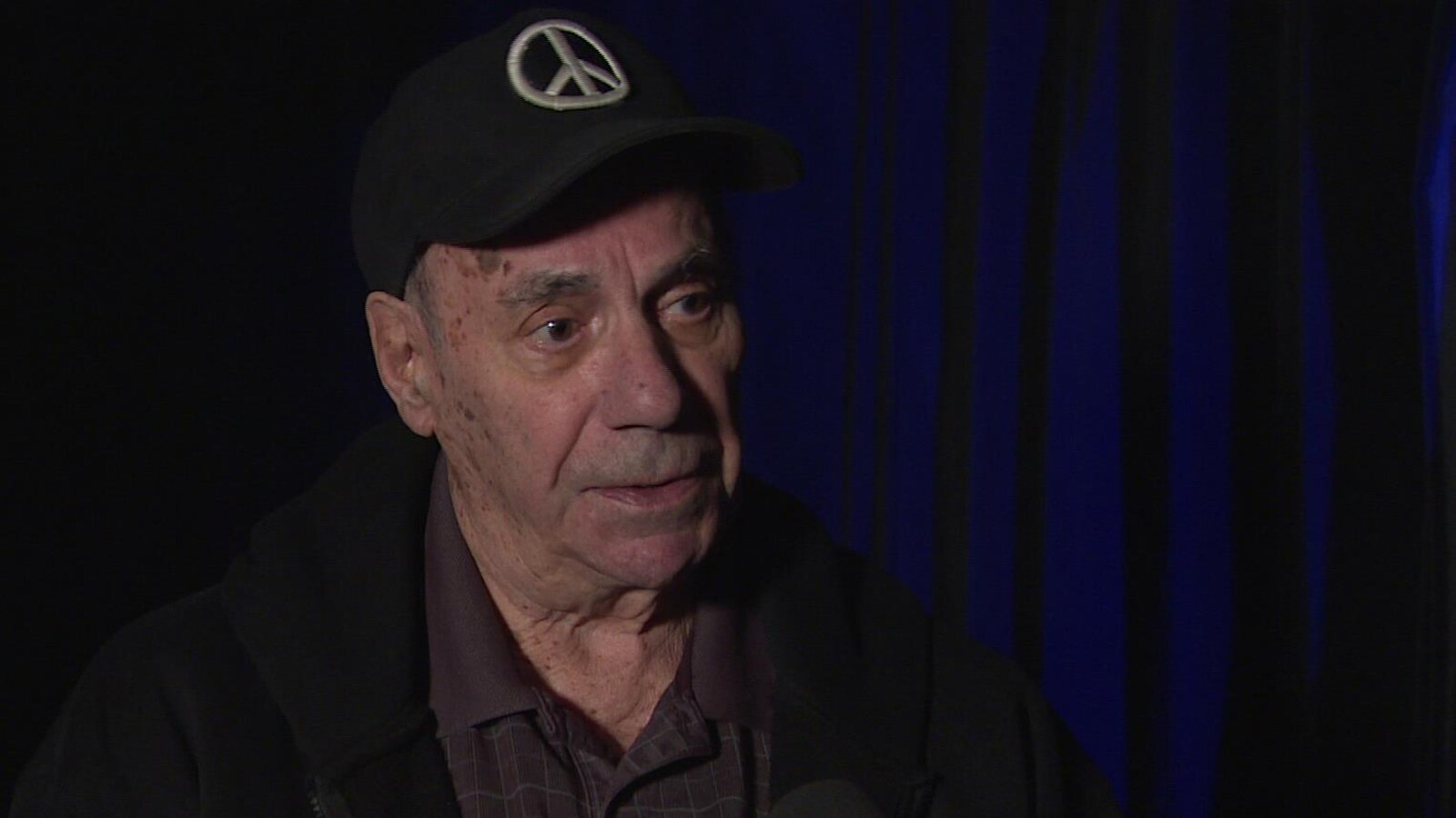 Un homme âgé et portant une casquette parle en entrevue.