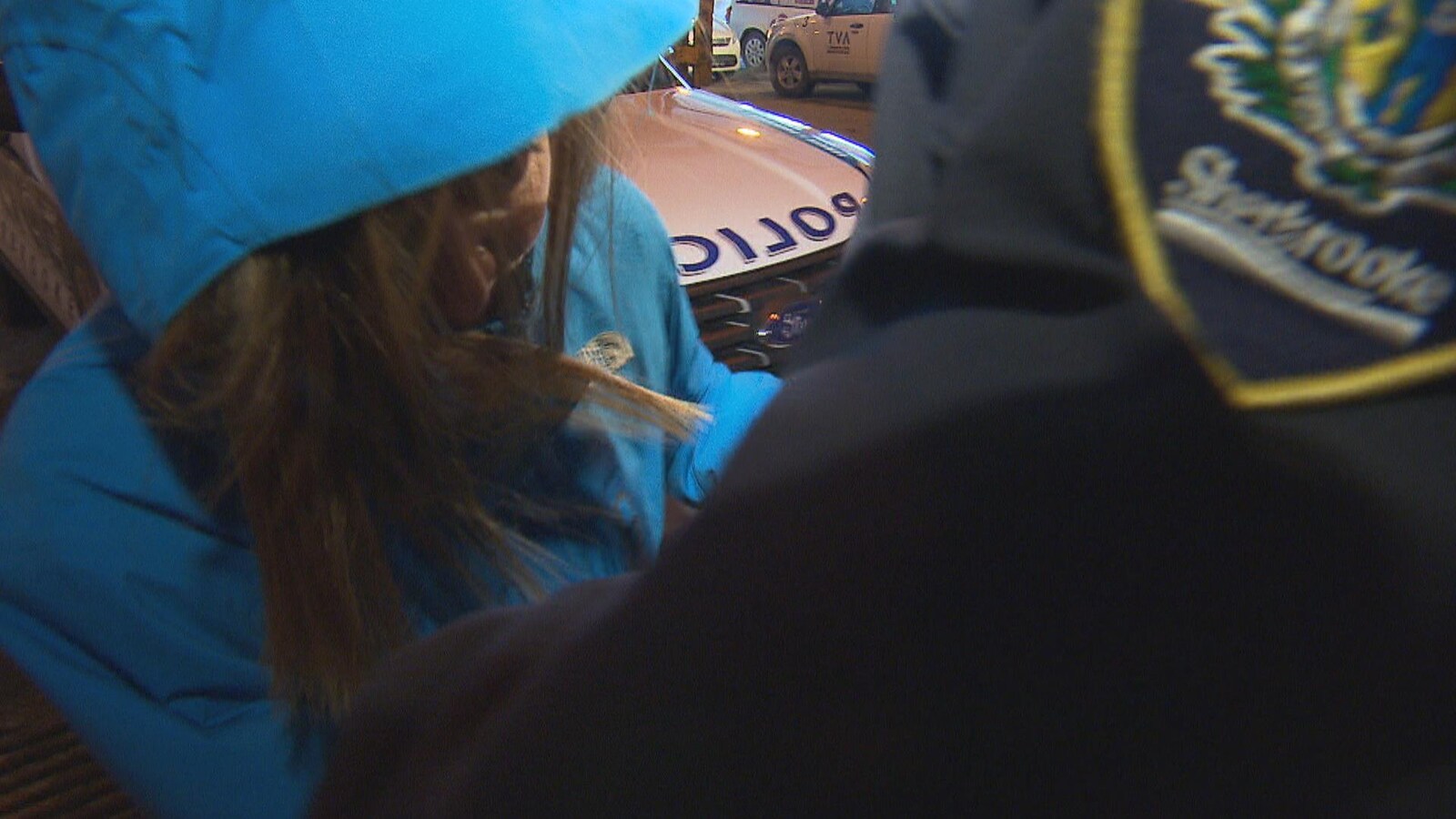 Une femme escortée par un policier masque son visage sous son capuchon.