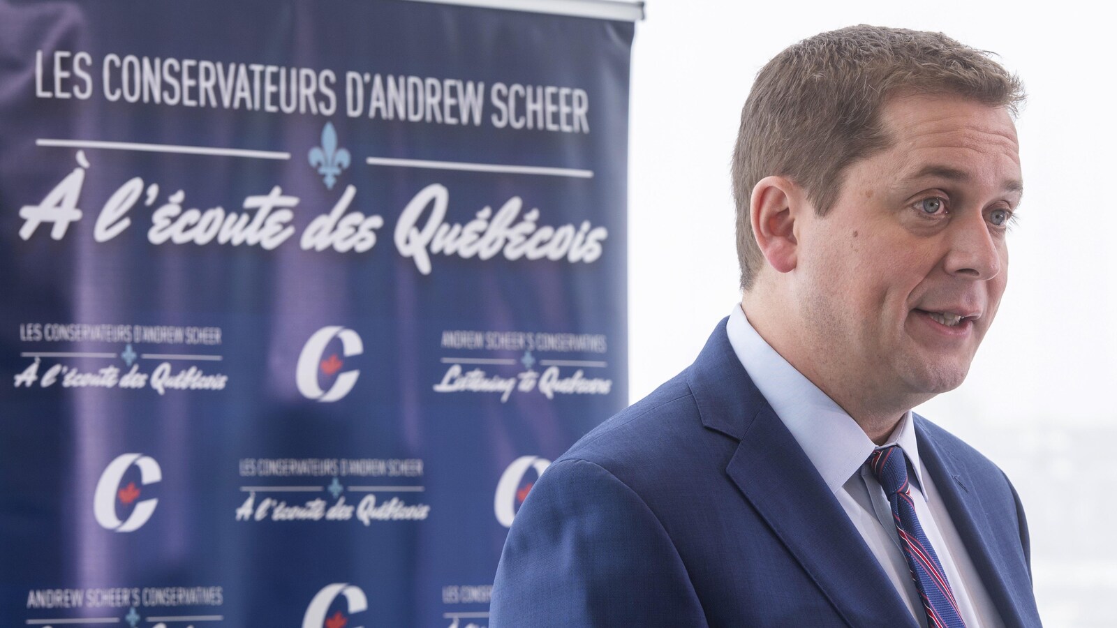 Andrew Scheer s'adresse aux médias lors d'une conférence de presse. Derrière lui, une bannière est suspendue. On peut y lire : « Les conservateurs d’Andrew Scheer à l’écoute des Québécois ».