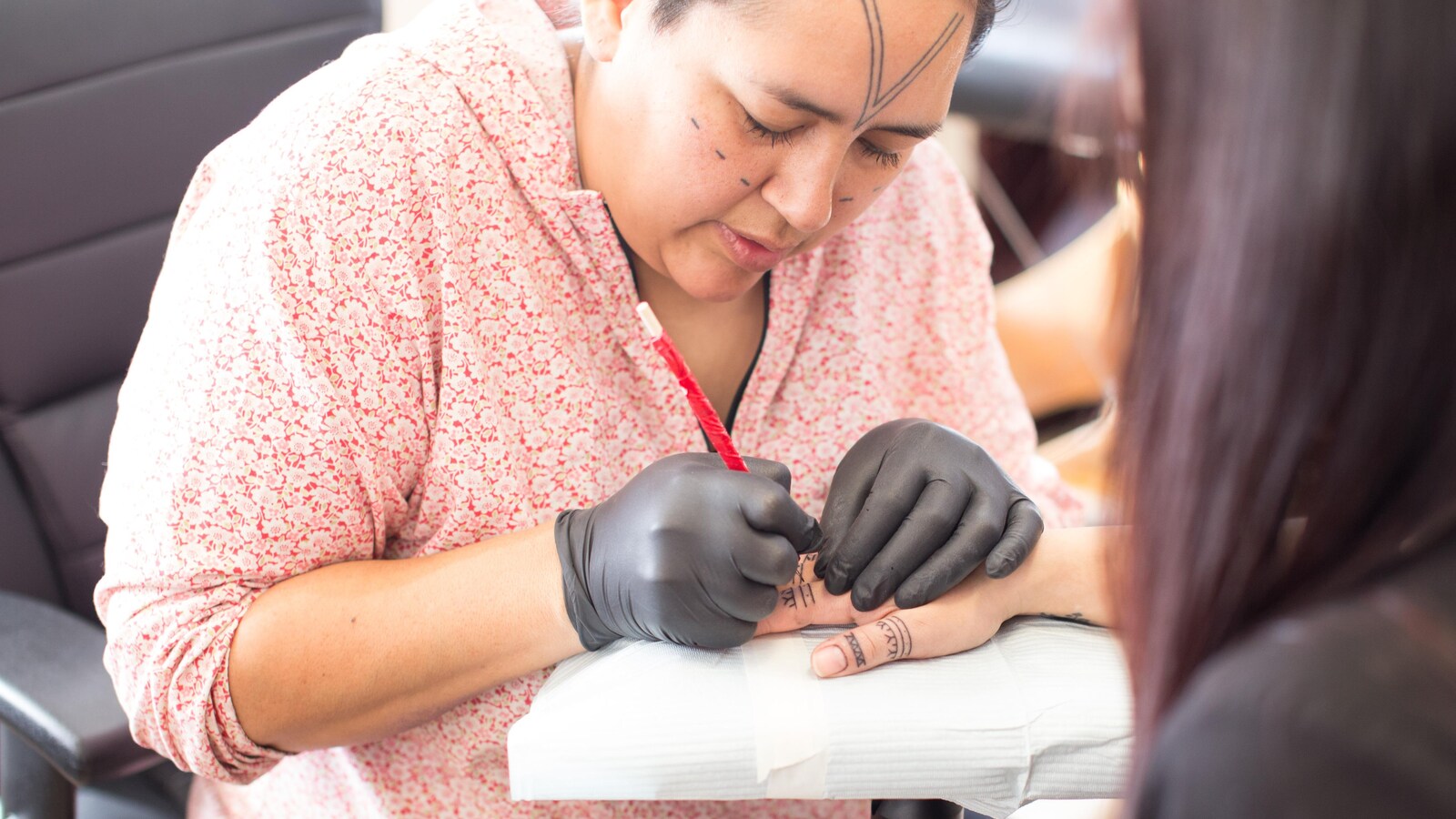 Angela Hovak Johnston tatouant la main d'une femme inuite selon la technique traditionnelle