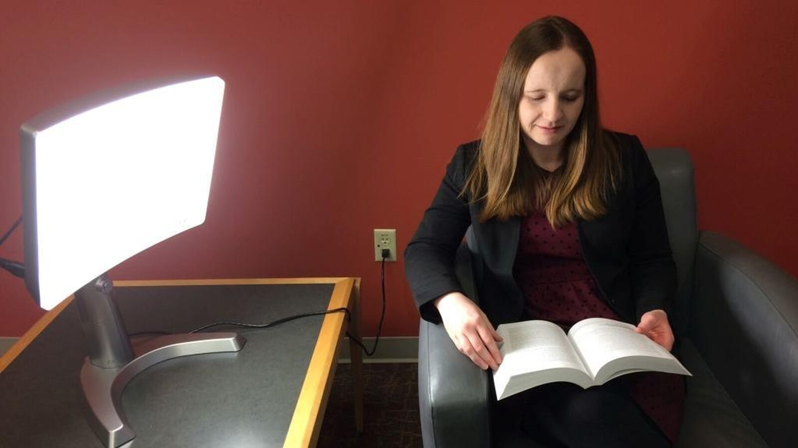 La directrice des services aux consommateurs à la bibliothèque municipale de London, Anne O'Sullivan lit au chevet d'une lampe de luminothérapie.
