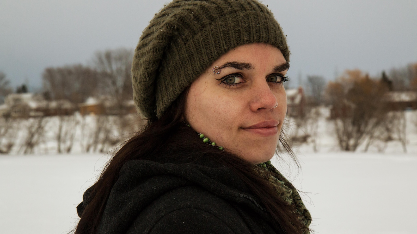 Portrait en couleur et en extérieur de l'auteure Annie Rousseau, devant un paysage enneigé. Elle porte une tuque, un foulard et des boucles d'oreilles vertes.
