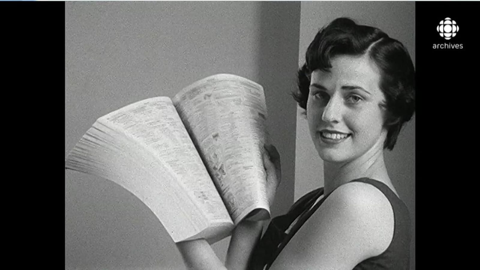 En noir et blanc, femme tout sourire posant avec un bottin téléphoniques ouvert entre ses mains,
