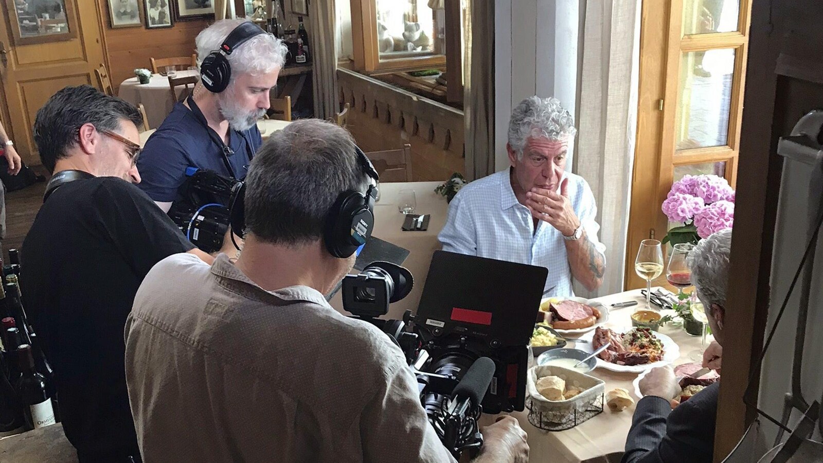 Anthony Bourdain mange avec quelqu'un, entouré de caméramans.