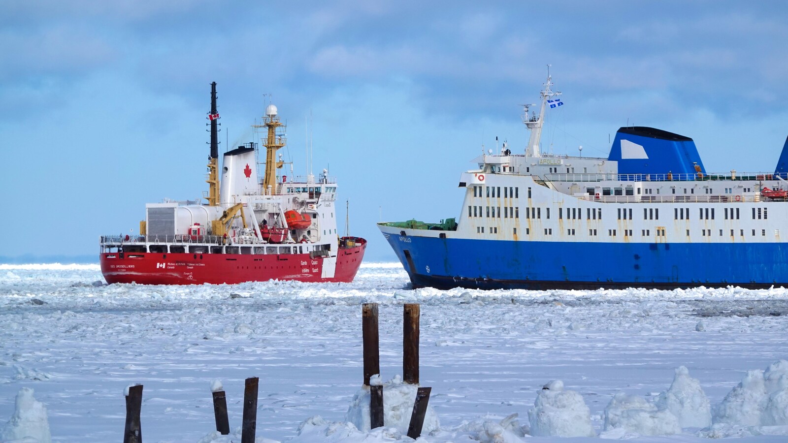 Deux navires se trouvent dans les eaux glacées d'un fleuve. Il s'agit d'un traversier et d'un brise-glace dans le fleuve Saint-Laurent en plein mois de février.