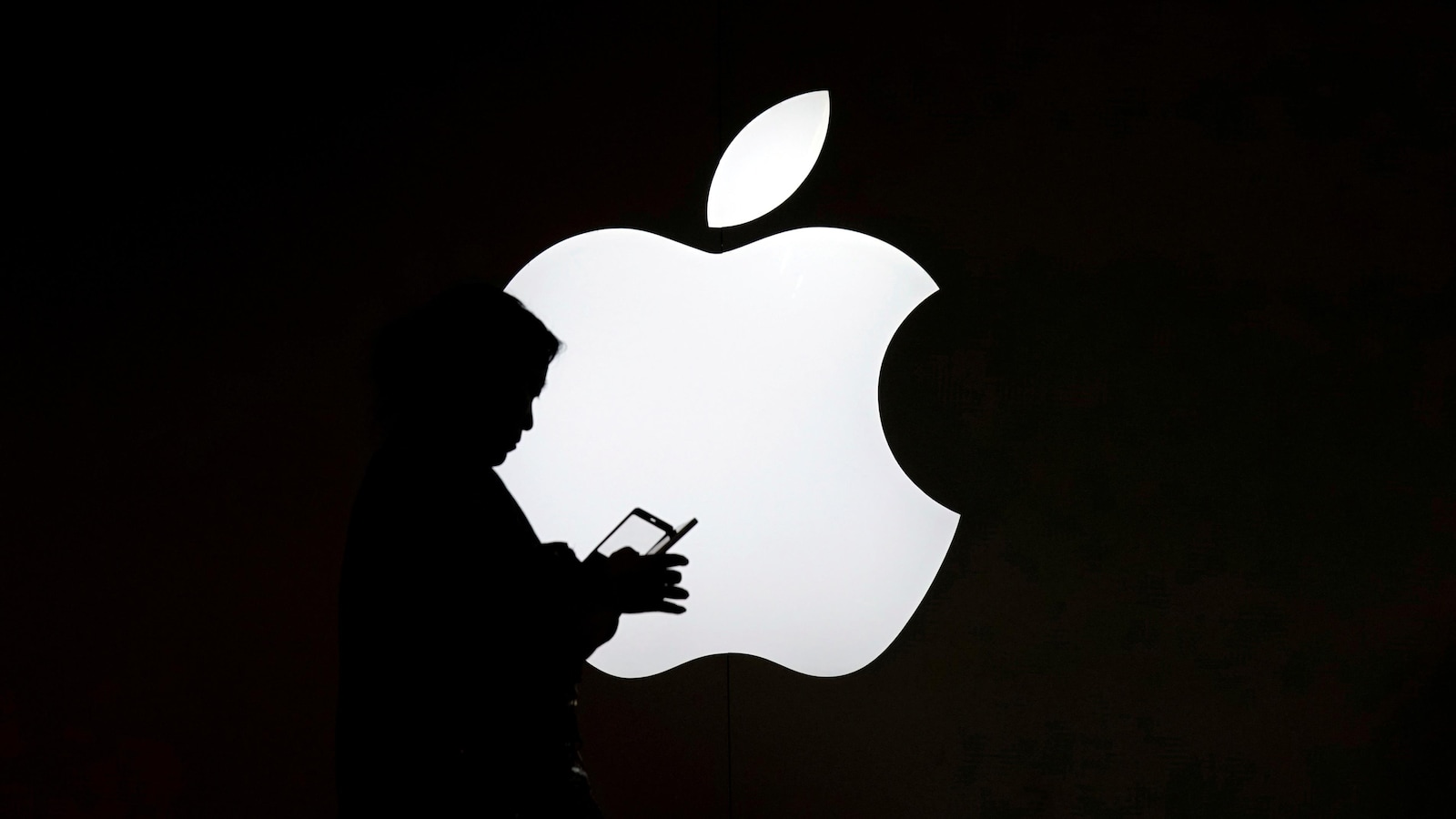 Une femme regarde l'écran de son téléphone portable devant un logo Apple.