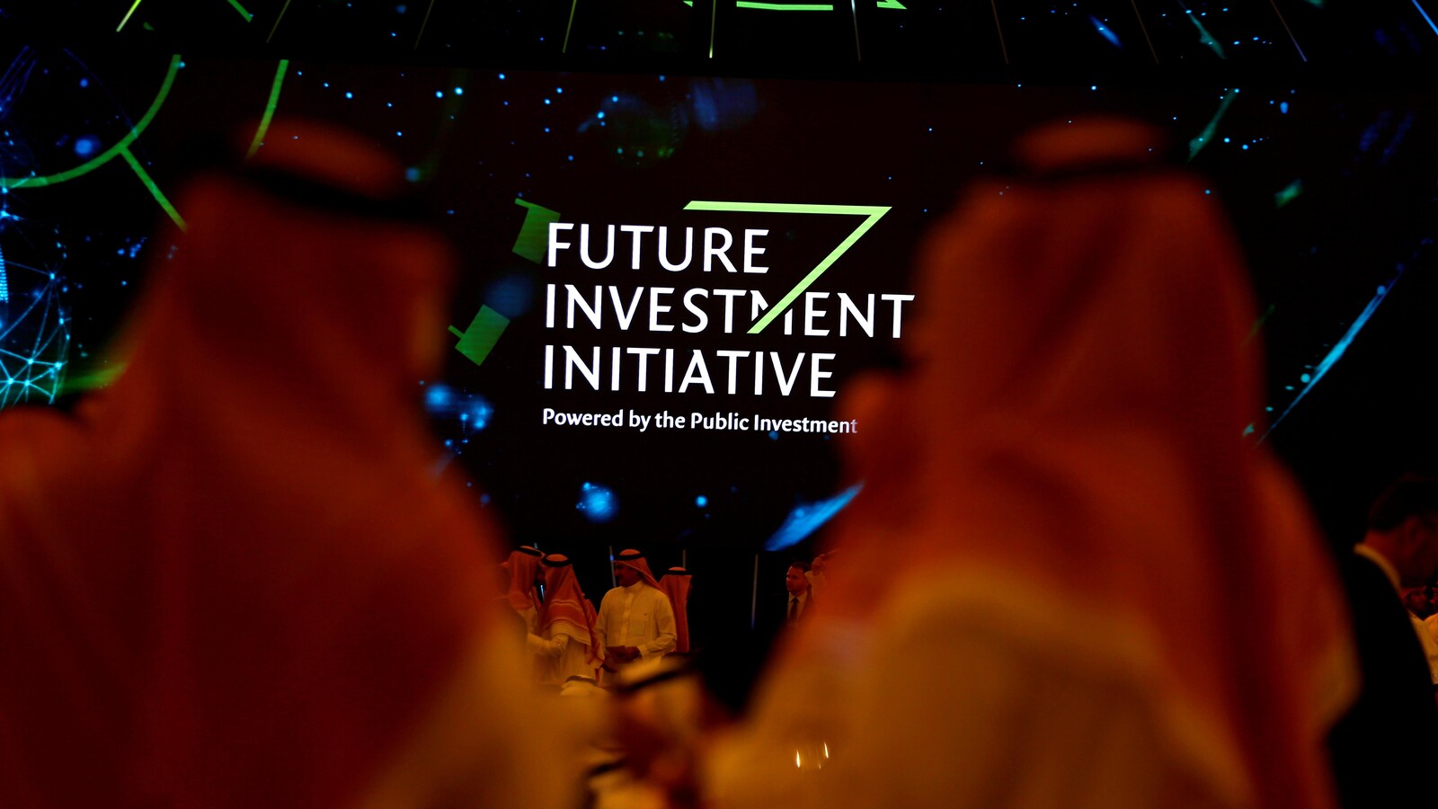 Des participants regroupés autour d'un panneau vantant un fonds d'investissement saoudien