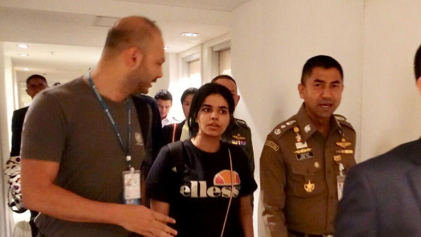 Une jeune femme circule dans un corridor, entourée de responsables et d'officiers en uniforme.