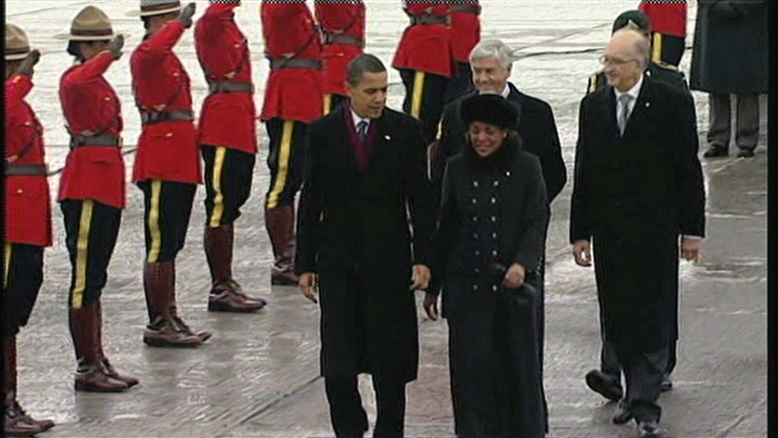 Barack Obama marche sur la piste de l'aéroport pendant que plusieurs officiers de la Gendarmerie Royale du Canada sont au garde-à-vous.