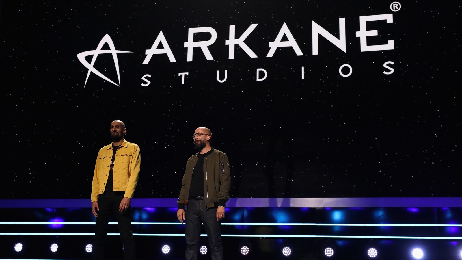 Deux hommes se tiennent debout sur une scène devant le logo d'Arkane Studios.
