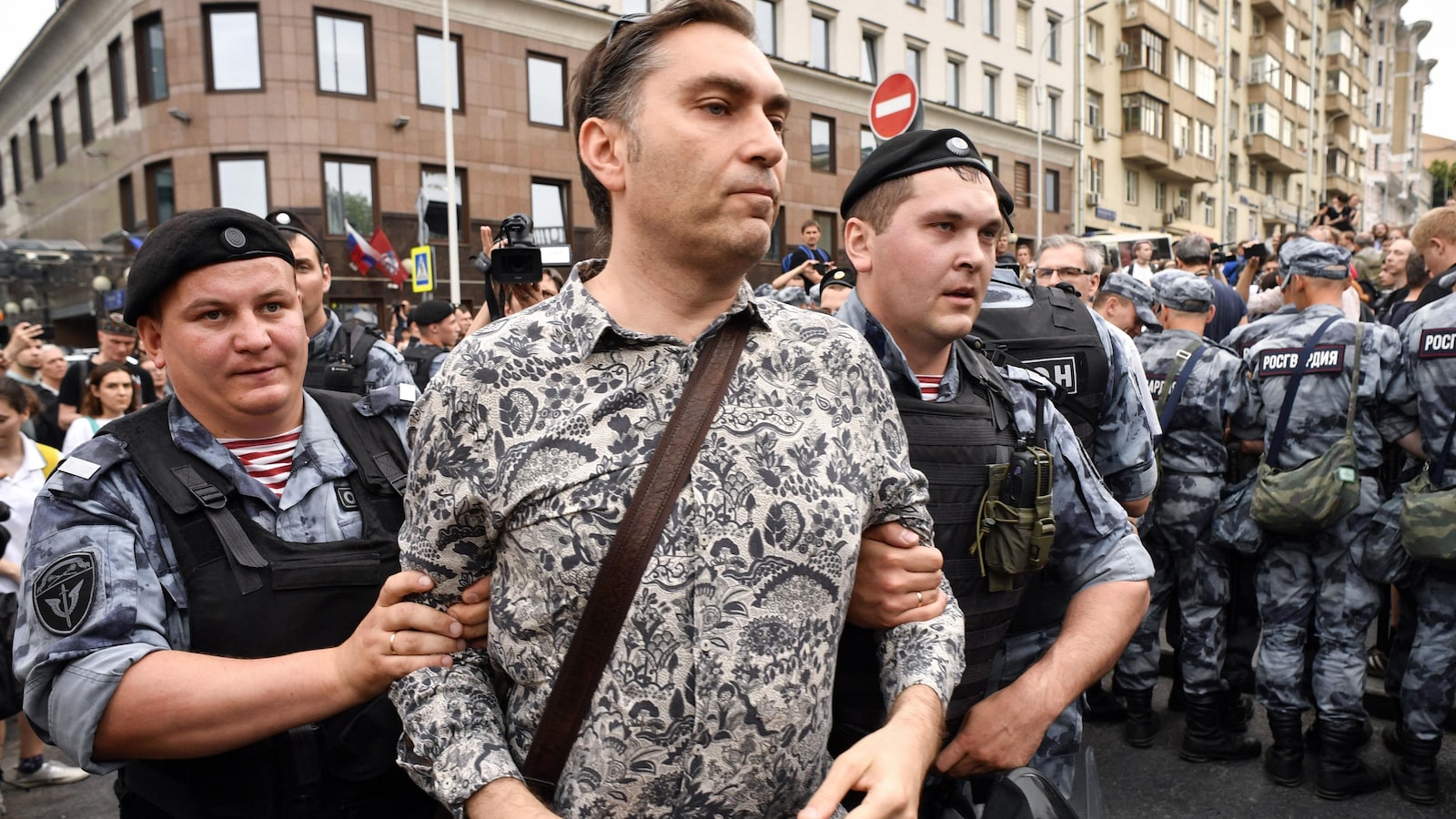 Deux policiers escortent un journaliste arrêté dans une foule.