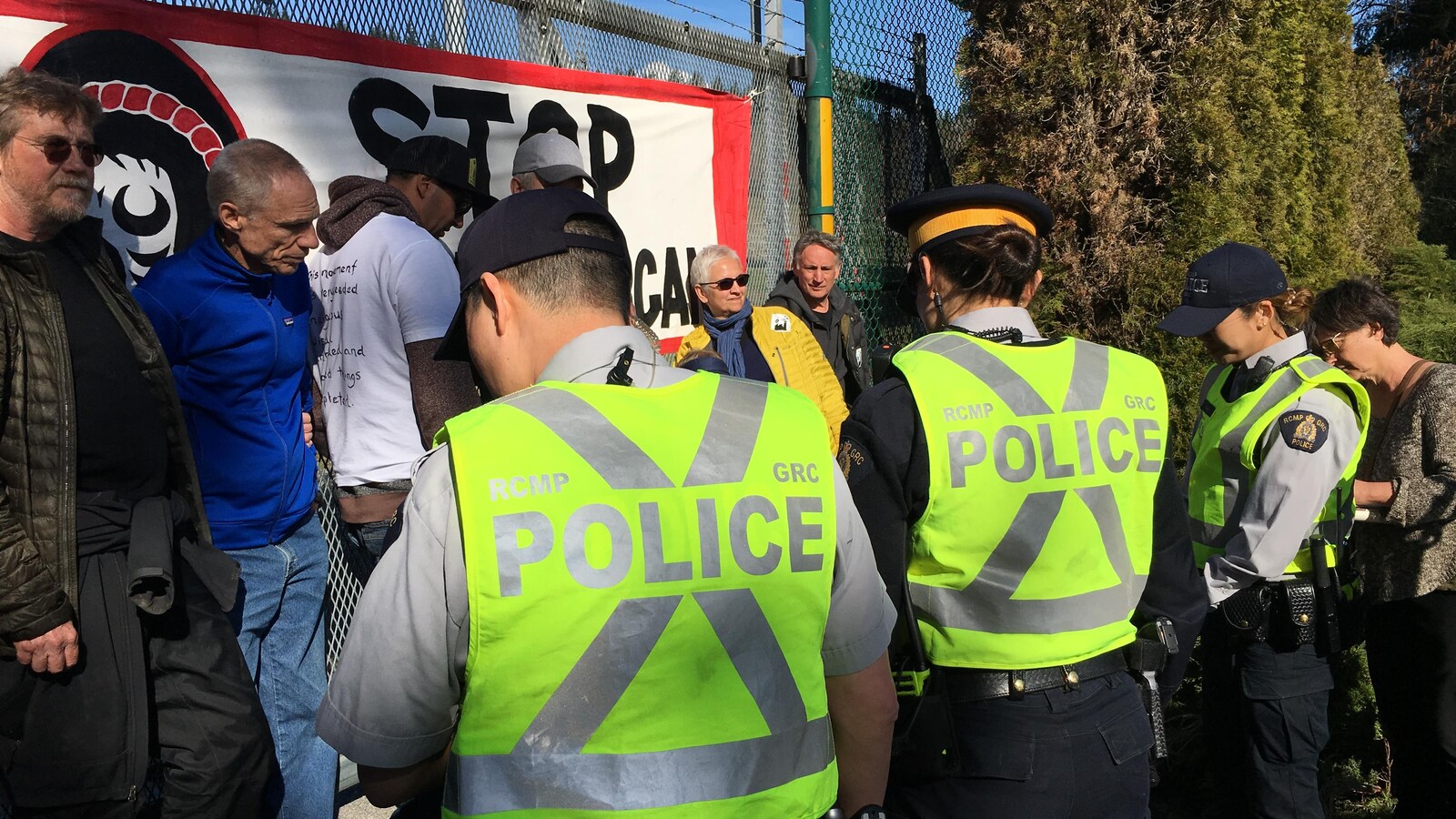 Des agents avec leur gilet jaune face à des opposants adossés à une barrière avec une bannière dessus.