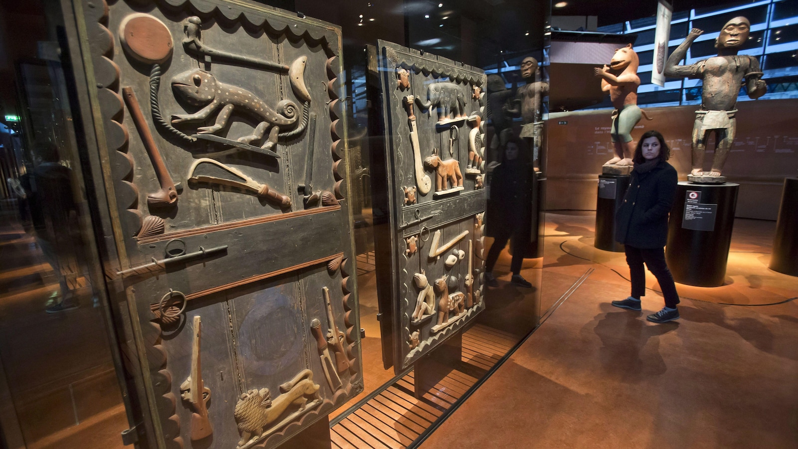 A visitor walks past a door of the king's palace Gele of the Dahomey kingdom, dated19th century, today's Benin, at Quai Branly museum in Paris, France, Friday, Nov. 23, 2018. From Senegal to Ethiopia, artists, governments and museums are eagerly awaiting a report commissioned by French President Emmanuel Macron on how former colonizers can return African art to Africa.(AP Photo/Michel Euler)