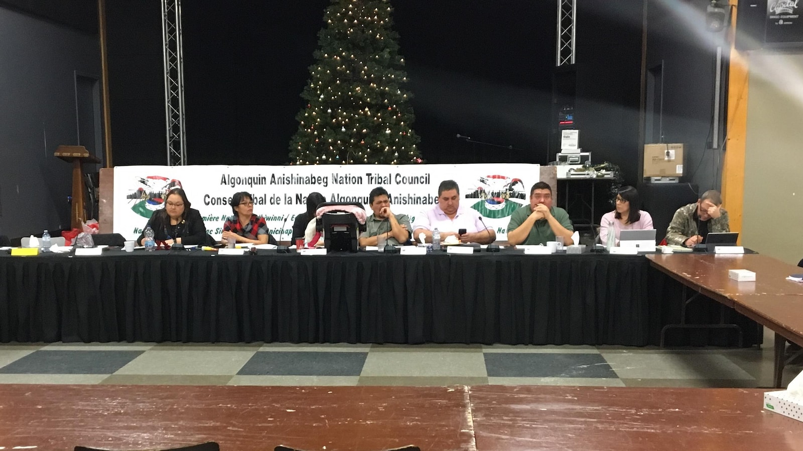 Des chefs algonquins sont assis derrière une longue table dans une salle communautaire.