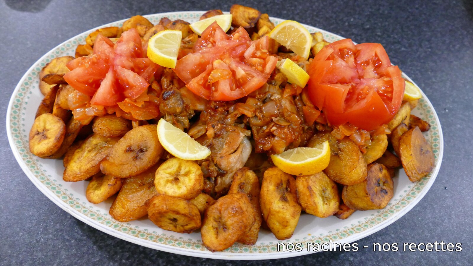 Dans une assiette de service, le poulet et les bananes plantains frites avec un décor de tomates fraîches et des quartiers de citron.