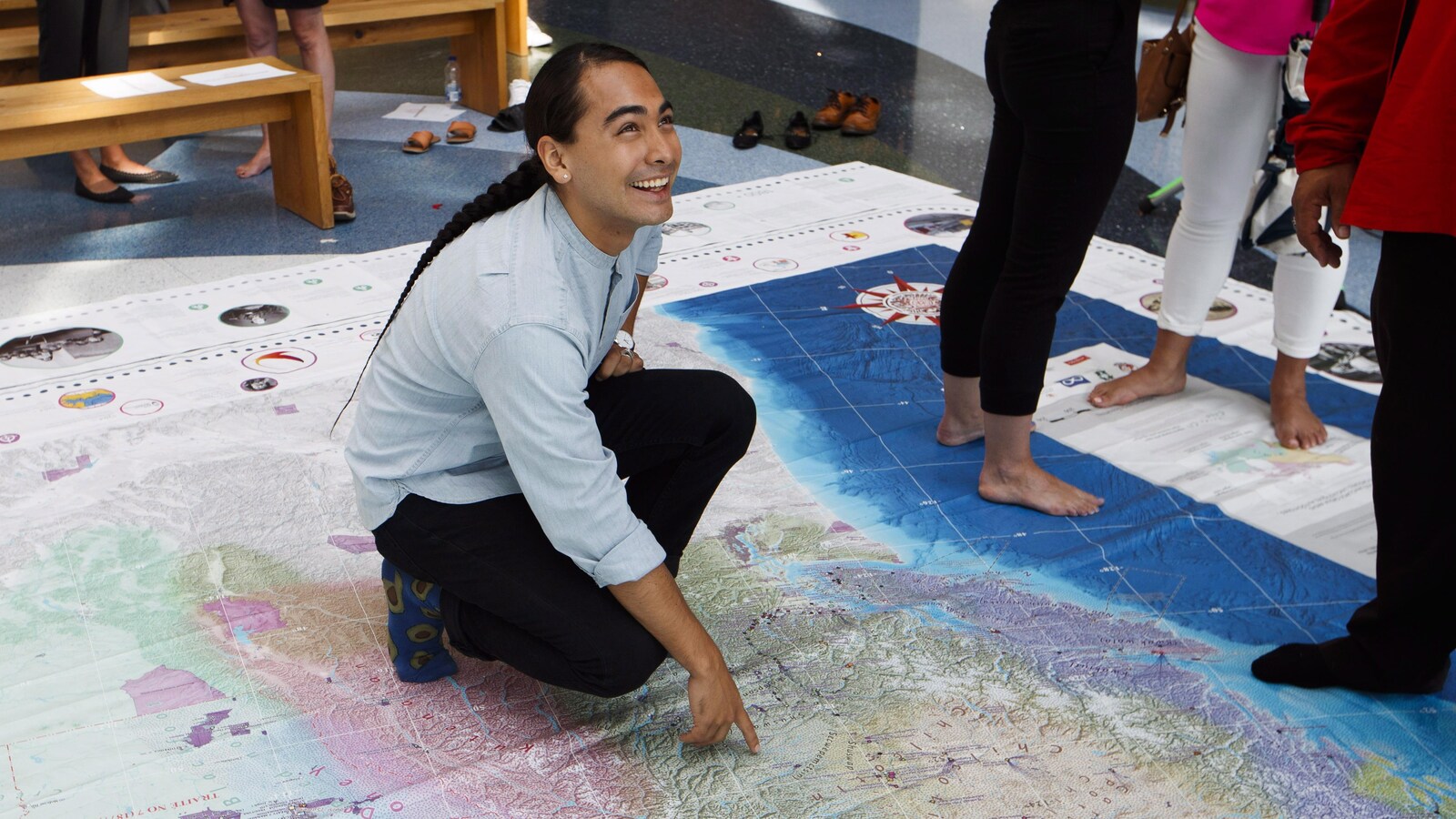 Julian Brave NoiseCat, souriant, montre un endroit sur la carte.