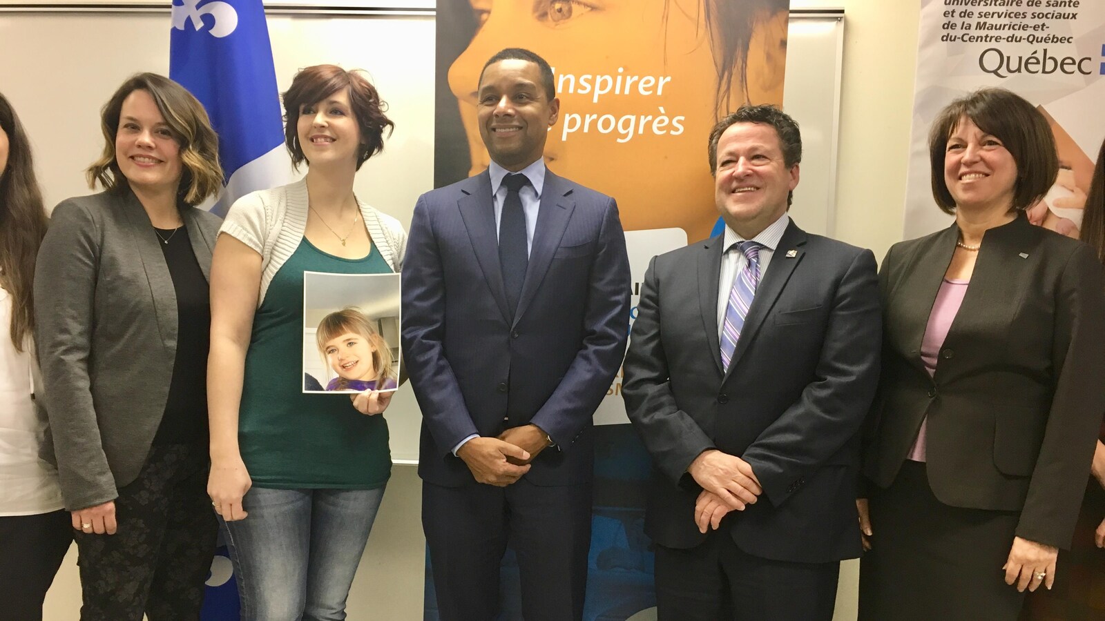 cinq personnes posent pour la caméra. Une dame tient une photo d'enfant dans ses mains.