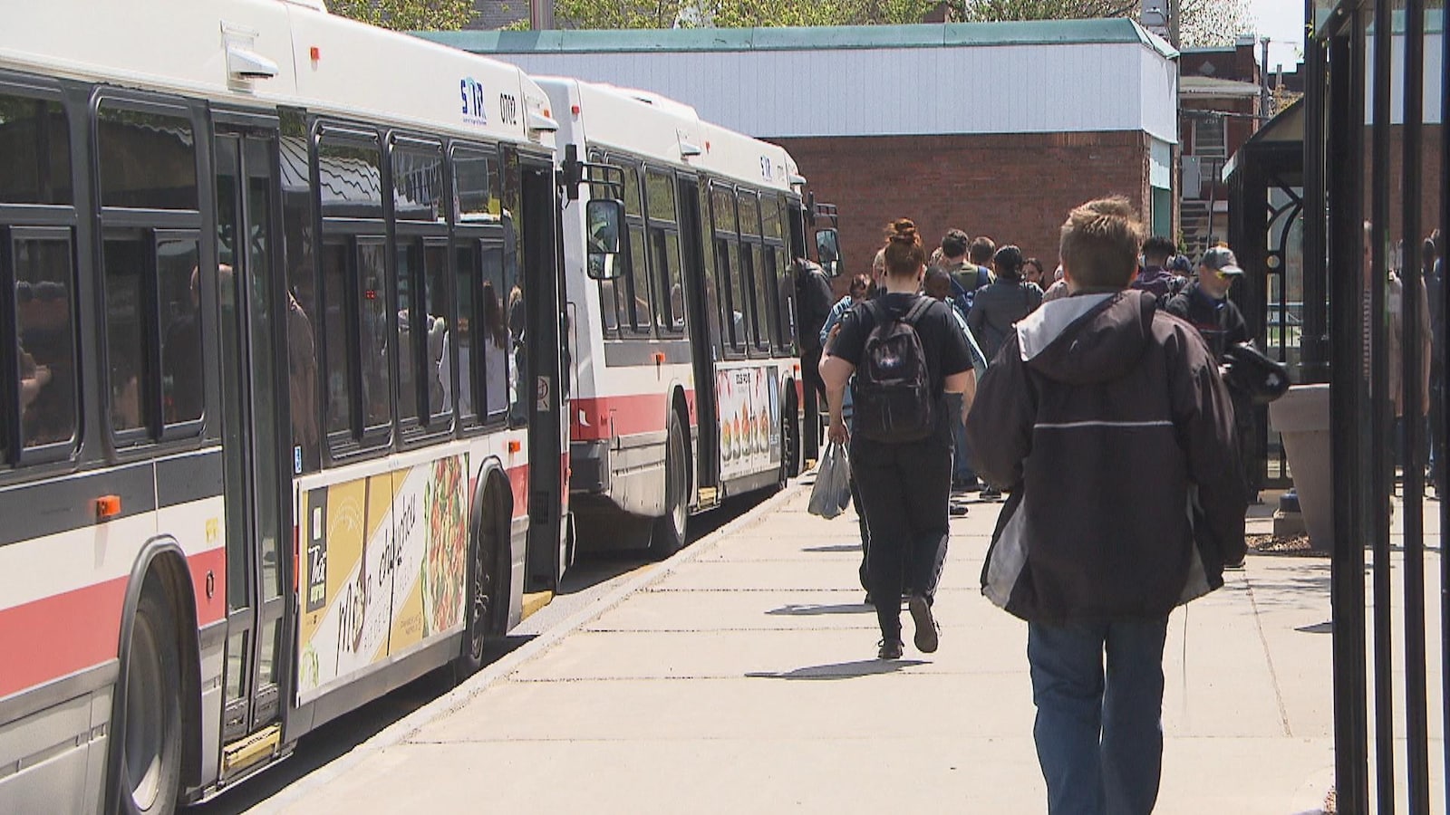 Des gens sur le quai qui embarquent dans des autobus au terminal du centre-ville de Trois-Rivières.