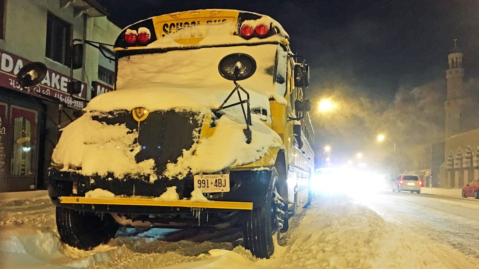 Photo d'un autobus jaune recouvert de neige garé le long d'une grande avenue.