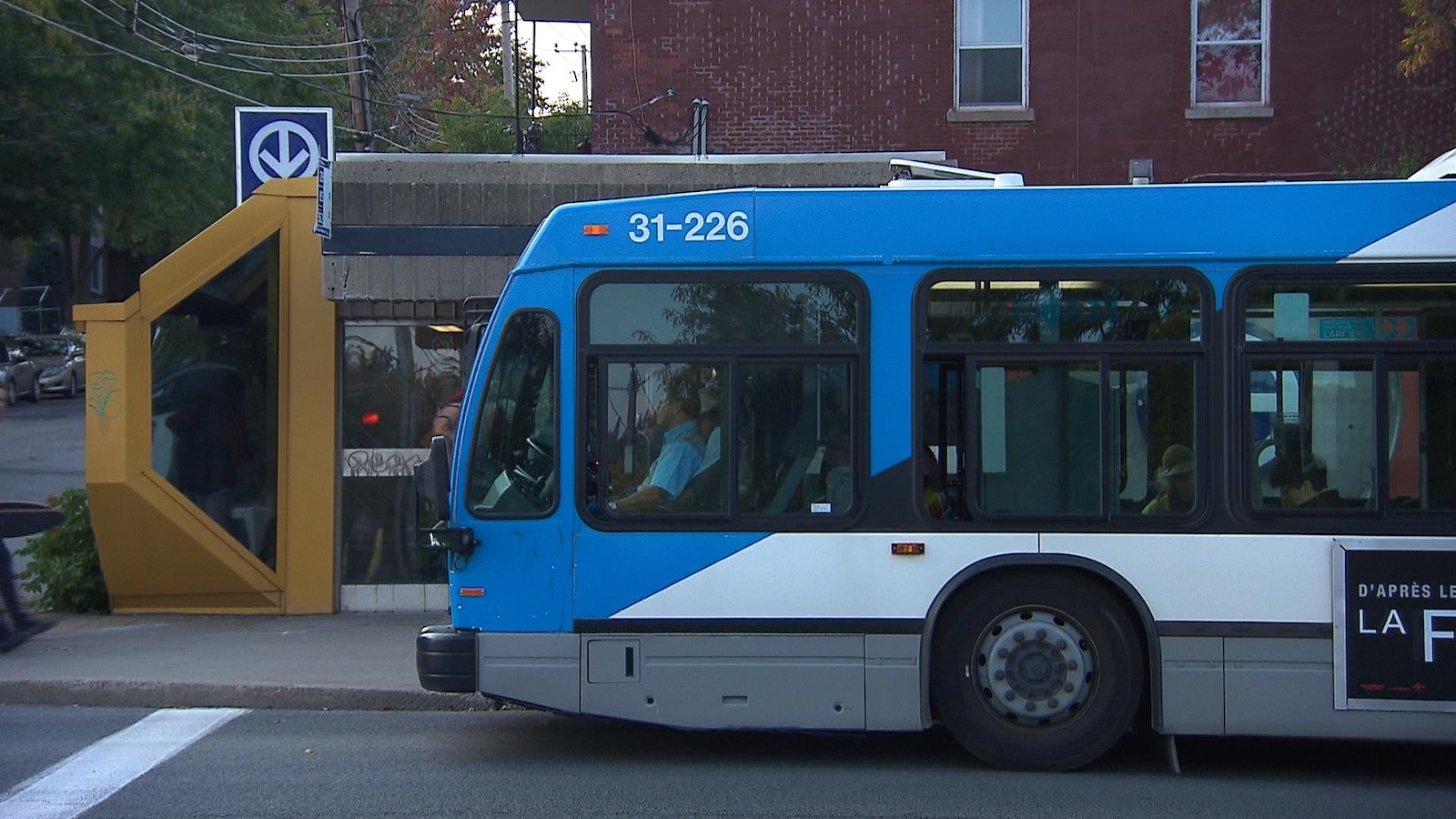 Un autobus arrêté à une station de métro du réseau de la STM, à Montréal. On voit le logo du métro de Montréal derrière l'entrée de la station.