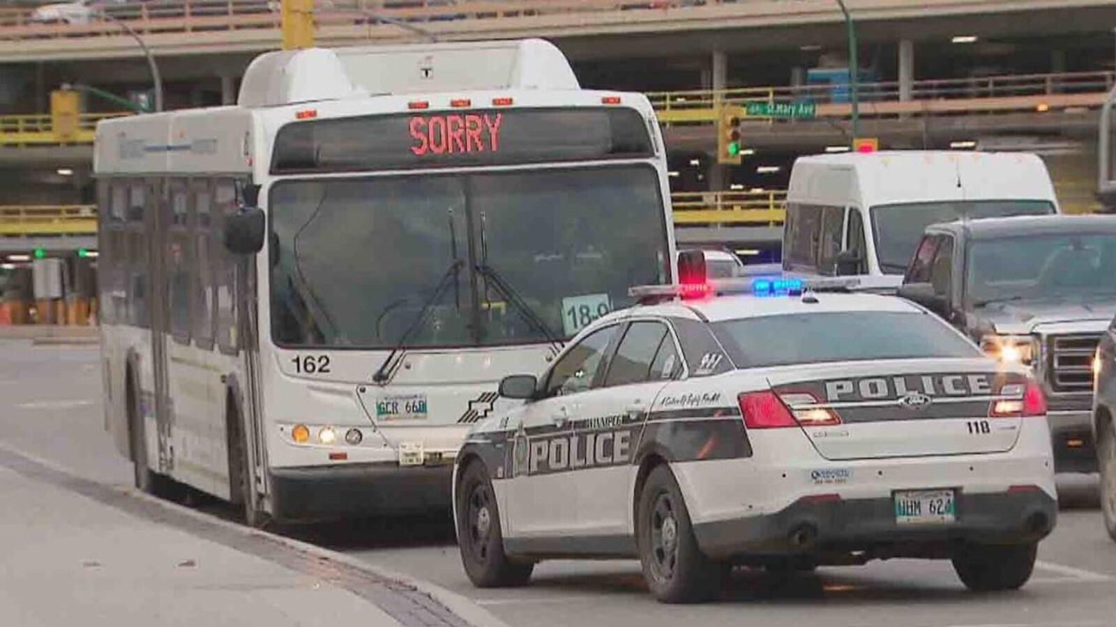 Un autobus est arrêté lelong d'un trottoir, et devant, ul y une voiture de police.