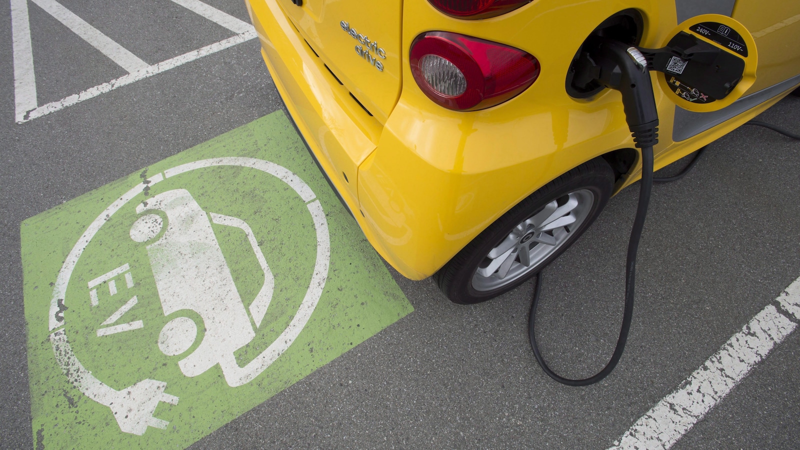 Une petite voiture électrique est rechargée dans un stationnement.