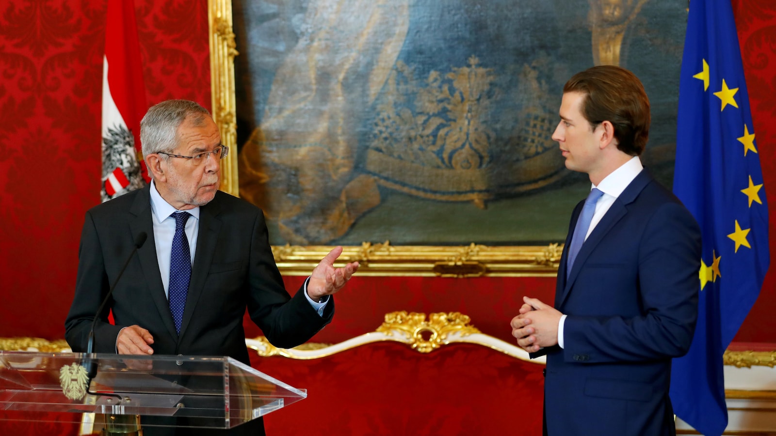 Les deux hommes se regardent devant un grand portrait et des drapeaux de l'Autriche et de l'Union européenne.