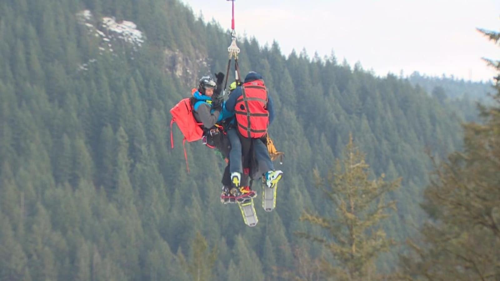 Trois hommes suspendus dans les airs par un harnais avec des arbres et des rochers en arrière plan.