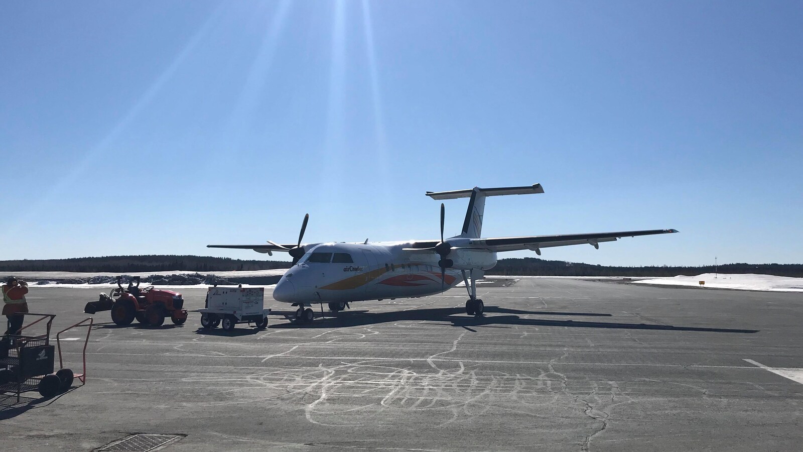 Un avion d'Air Creebec est immobile, un employé de l'aéroport observe l'appareil.
