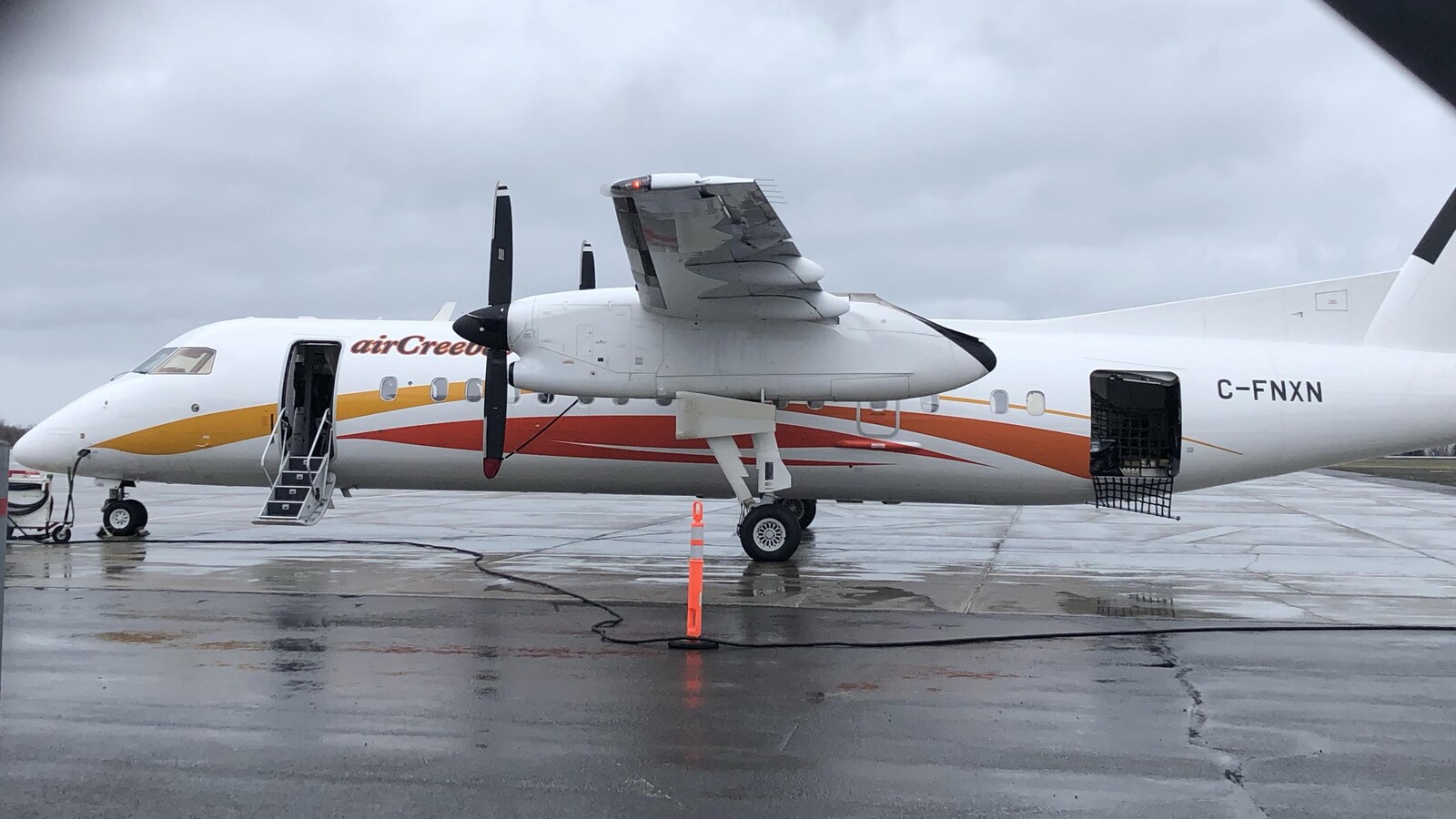 Un avion se trouve sur une piste d'atterrissage d'un aéroport. Un cône orange se situe à côté de l'appareil.