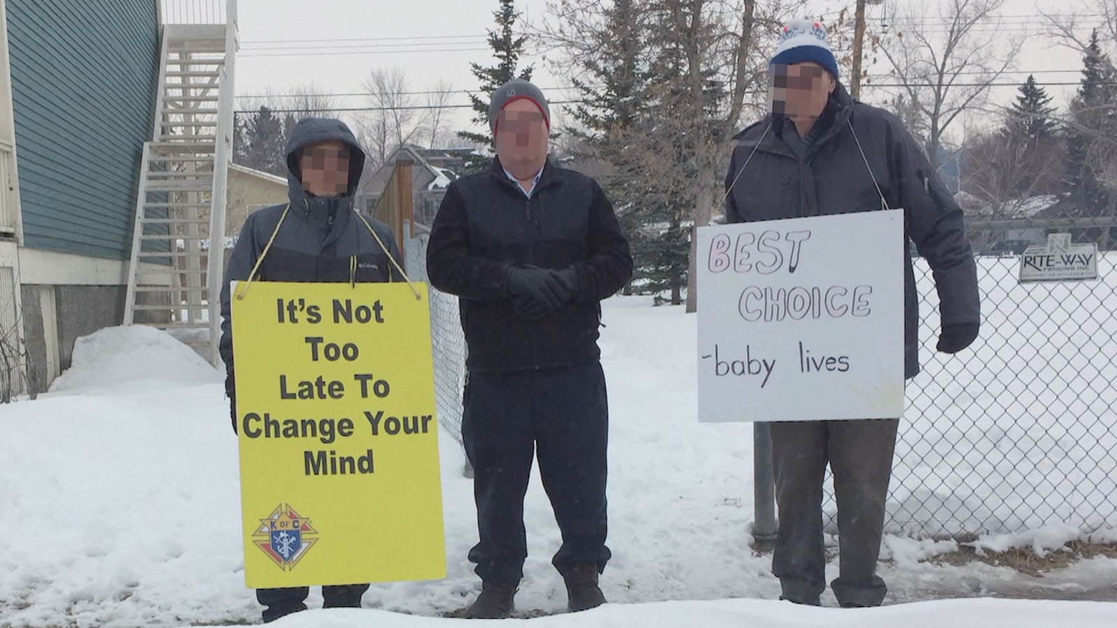 Trois hommes se tiennent debout à proximité de la clinique Kensignton de Calgary. Deux d'entre eux portent des pancartes invitant les patientes à renoncer à l'avortement.