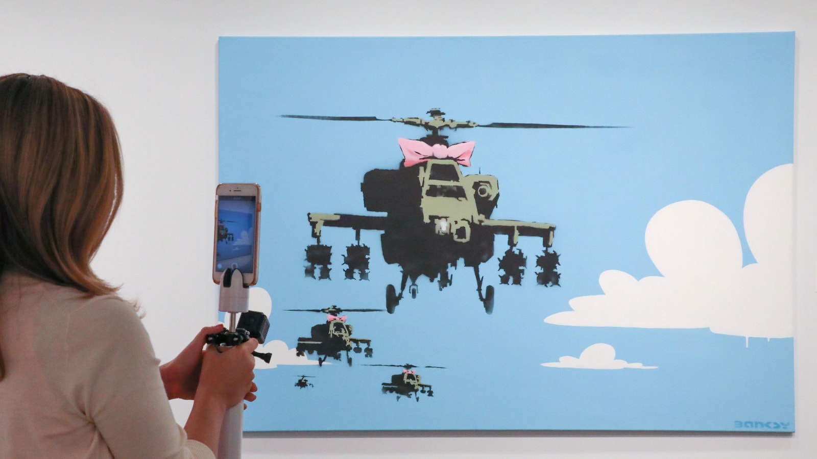 La toile « Happy Choppers » présente des hélicoptères militaires habillés d'un noeud rose et volant dans le ciel.