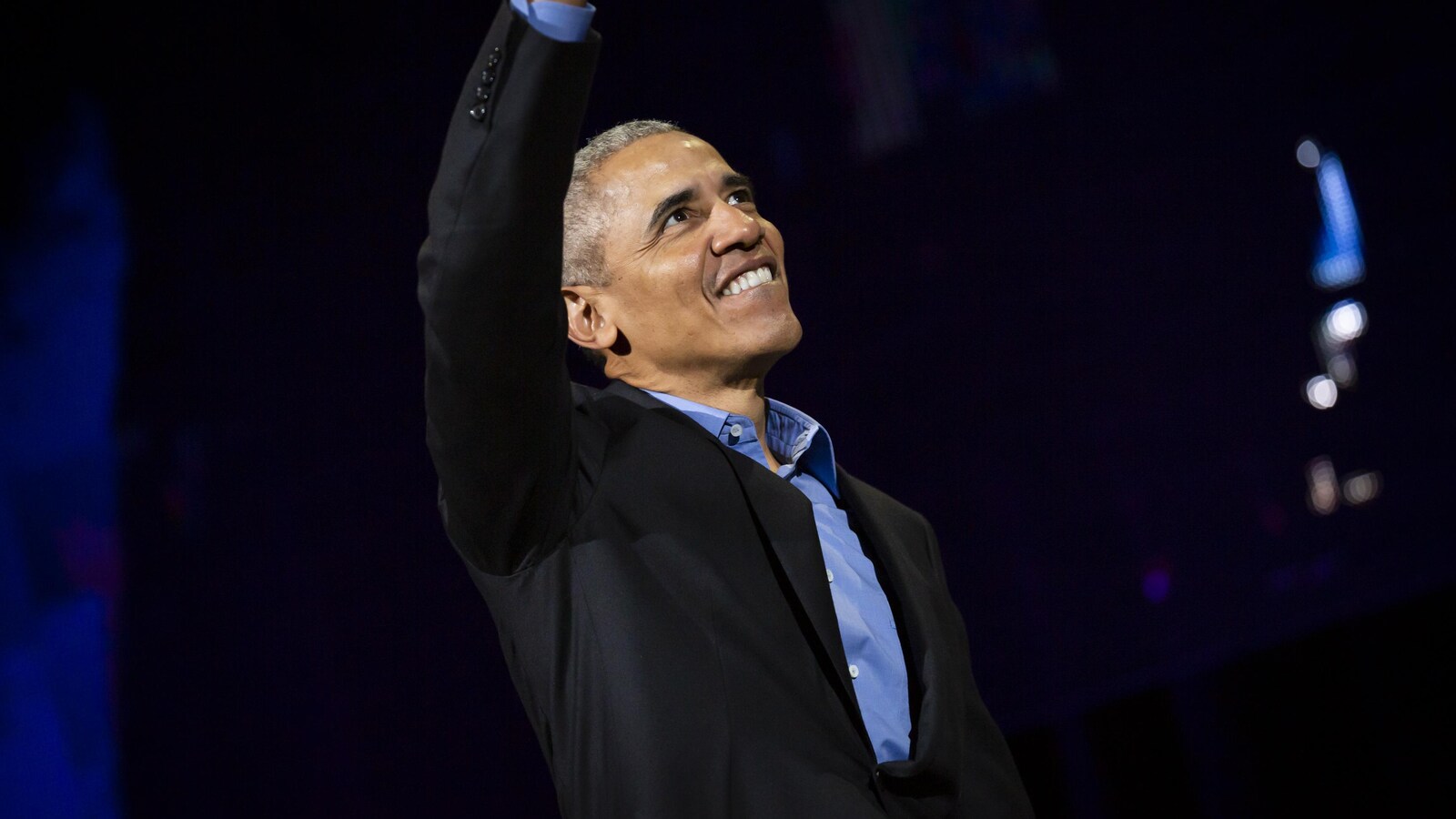 Barack Obama salue la foule, un bras dans les airs et un grand sourire aux lèvres.