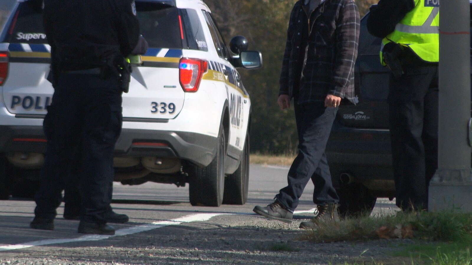 Un homme inconnu lève sa jambe gauche pour tester son équilibre devant trois agents du Service de police de la Ville de Gatineau en bordure de la route.