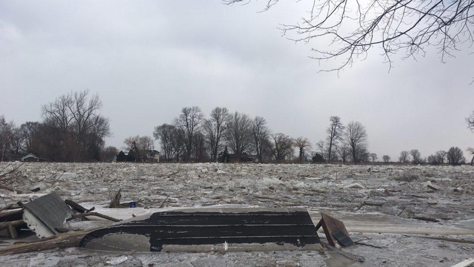 Un bateau et des débris transportés par une rivière qui sort de son lit.