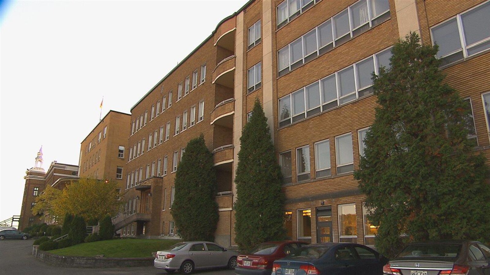 Un bâtiment en brique compte cinq étages. Il y a des véhicules stationnés devant.