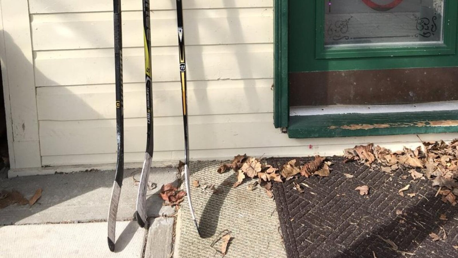 Trois bâtons de hockey à côté d'une porte d'entrée.