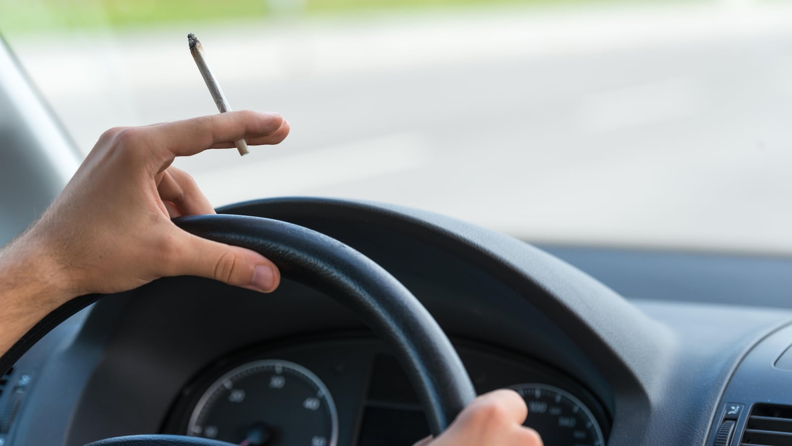 Un conducteur tient son volant avec un joint de cannabis à la main.